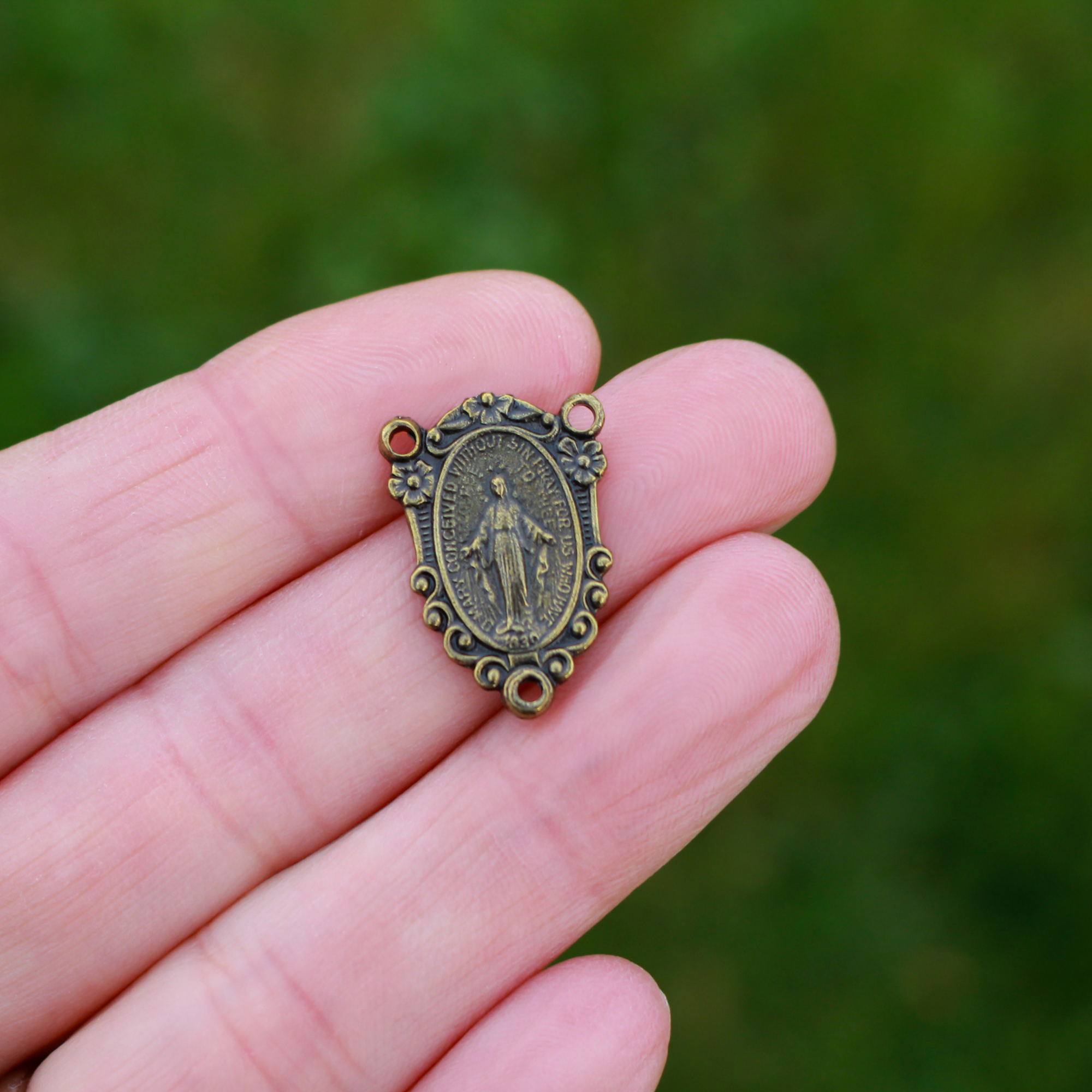 Miraculous Mary rosary centerpiece in an antiqued bronze finish and ornate flower border.